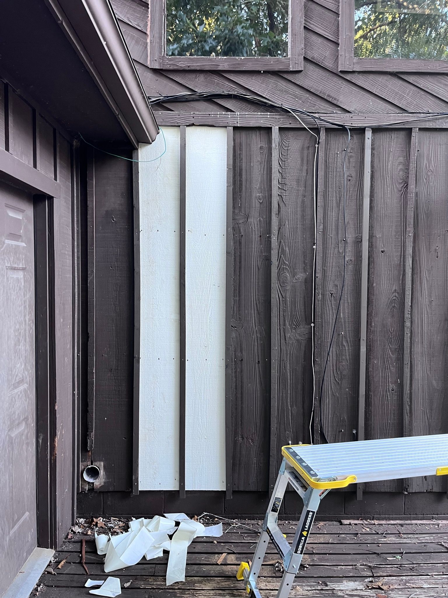Exterior wall with weathered wood siding. A vertical section is unfinished and silver. A step stool sits below.