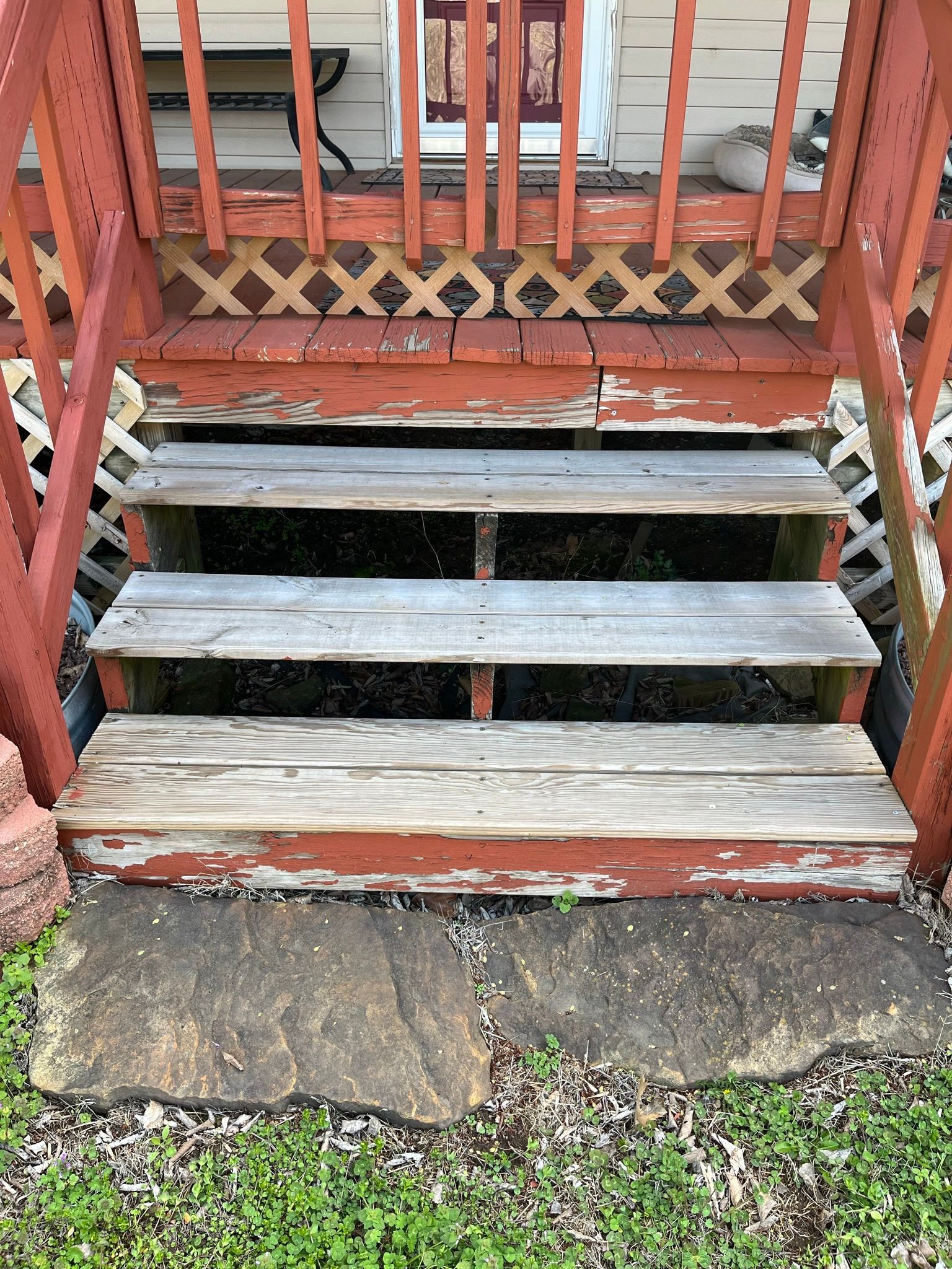 Wooden porch steps with peeling paint, leading to a door with a lattice design, situated outdoors.