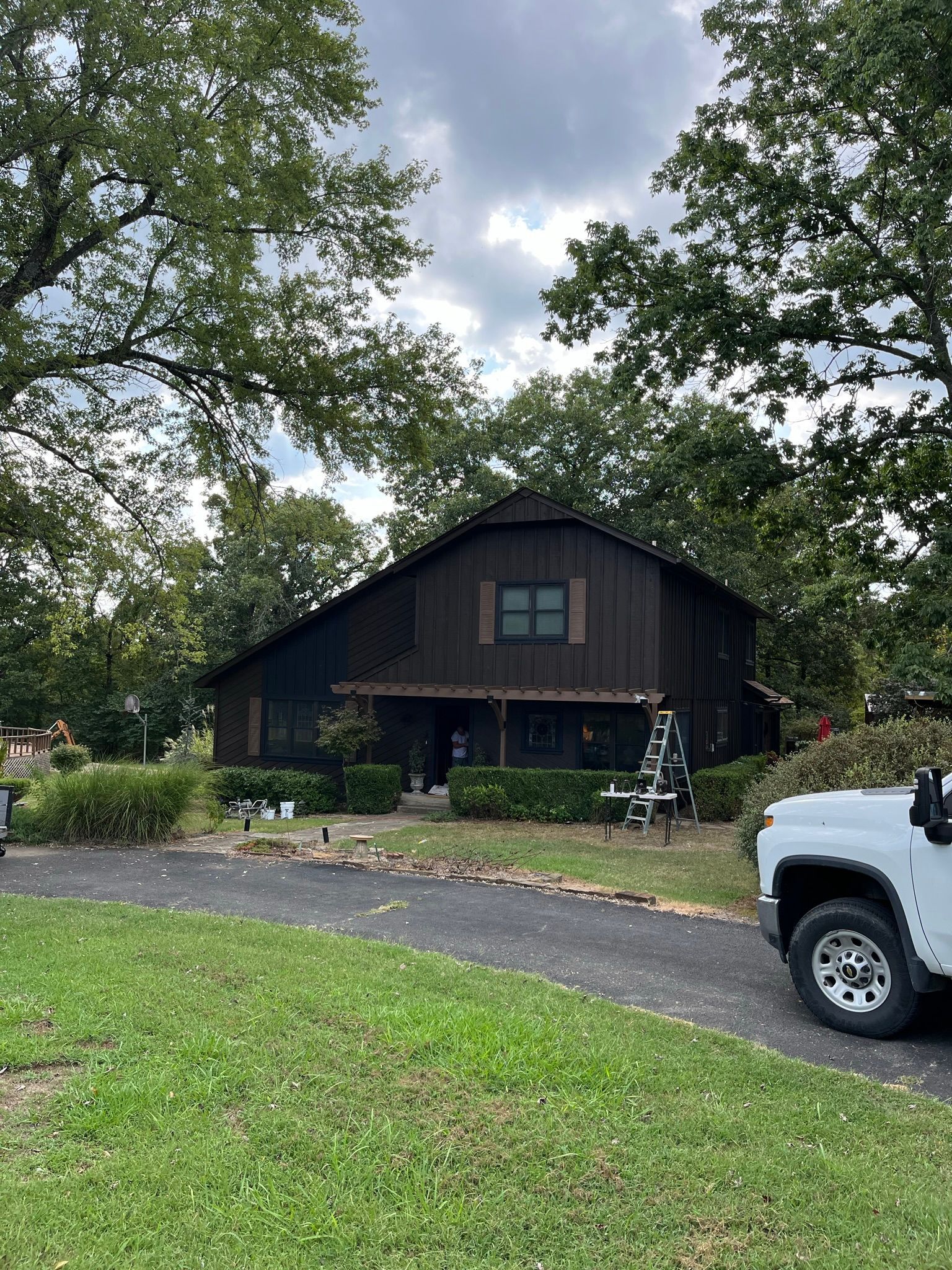 Brown house with a curved roof, surrounded by trees. A pickup truck is parked in the driveway.