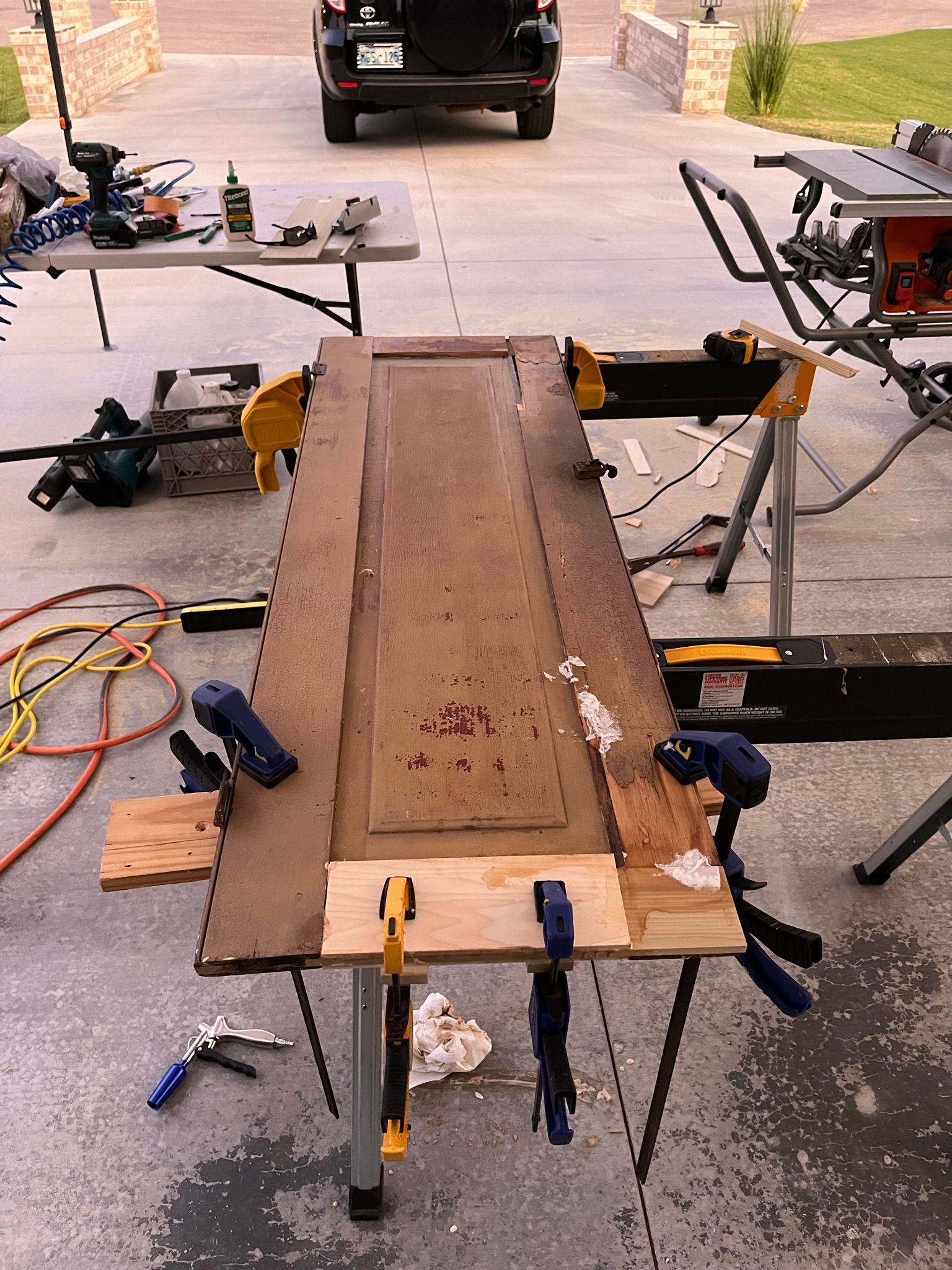 Door being repaired on a work table with clamps and tools in an outdoor setting.