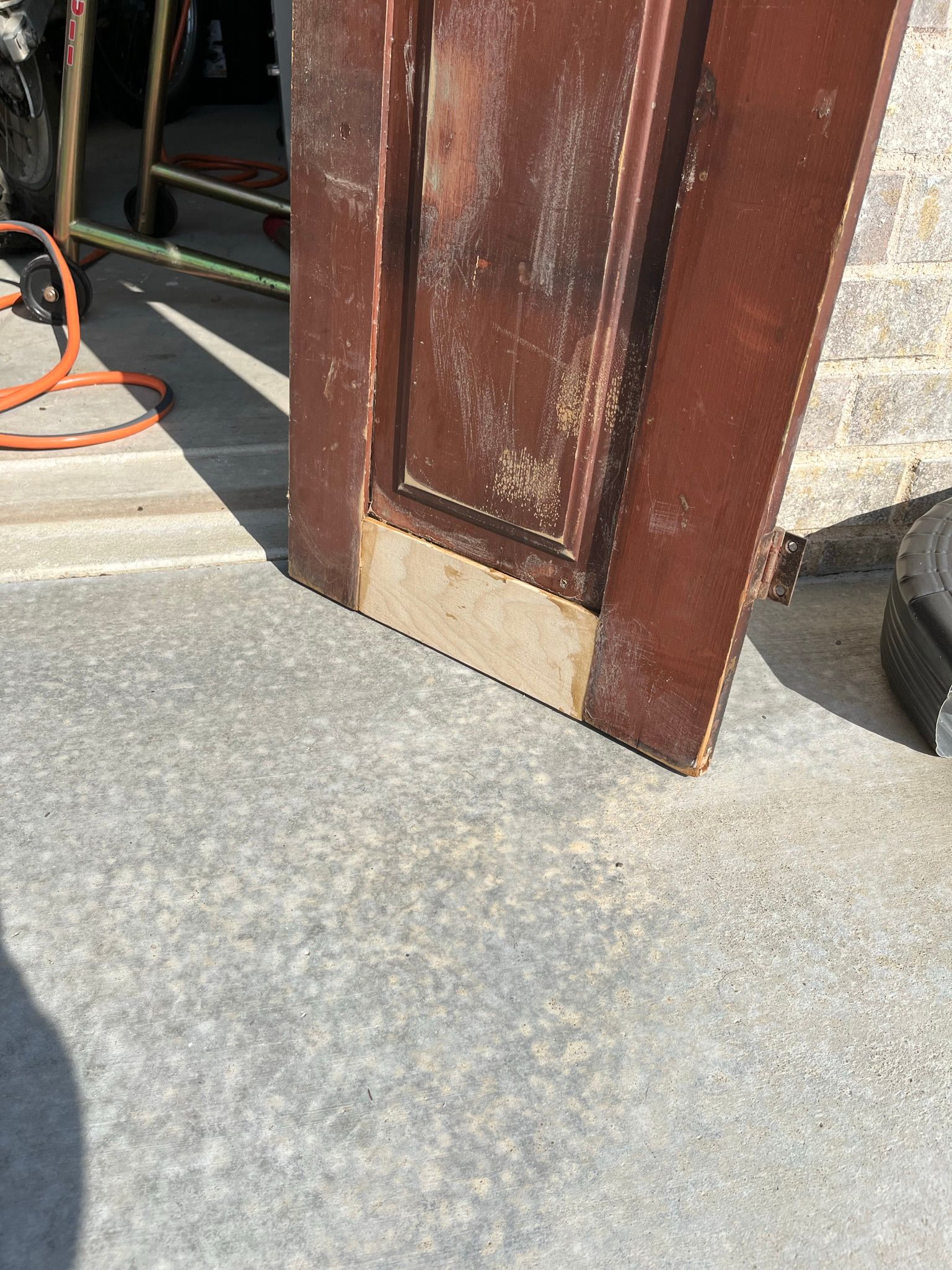Old brown wooden door propped up on a gray concrete surface, showing wear and tear.