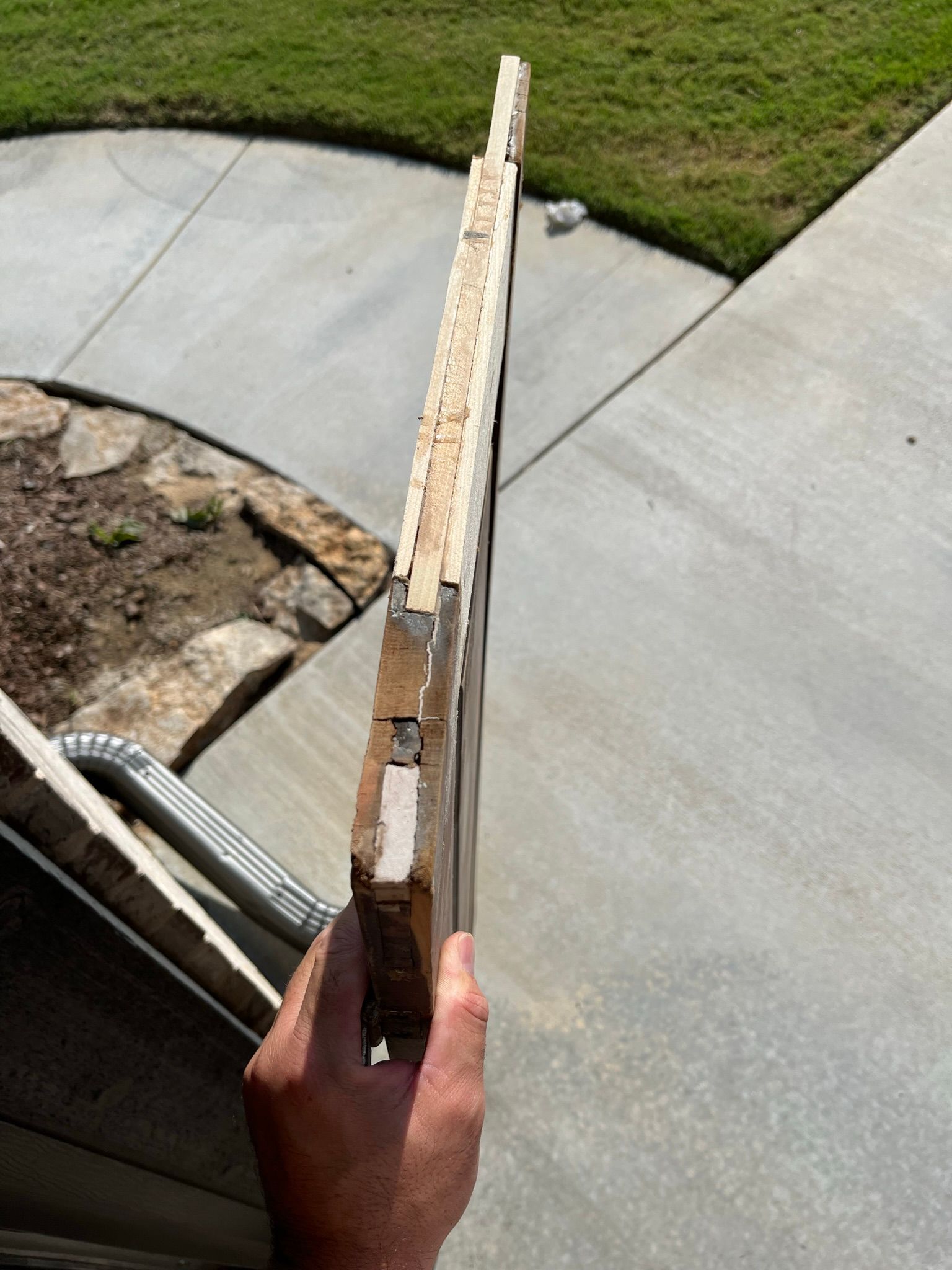 Person holding a damaged wooden door frame outdoors on a sunny day.