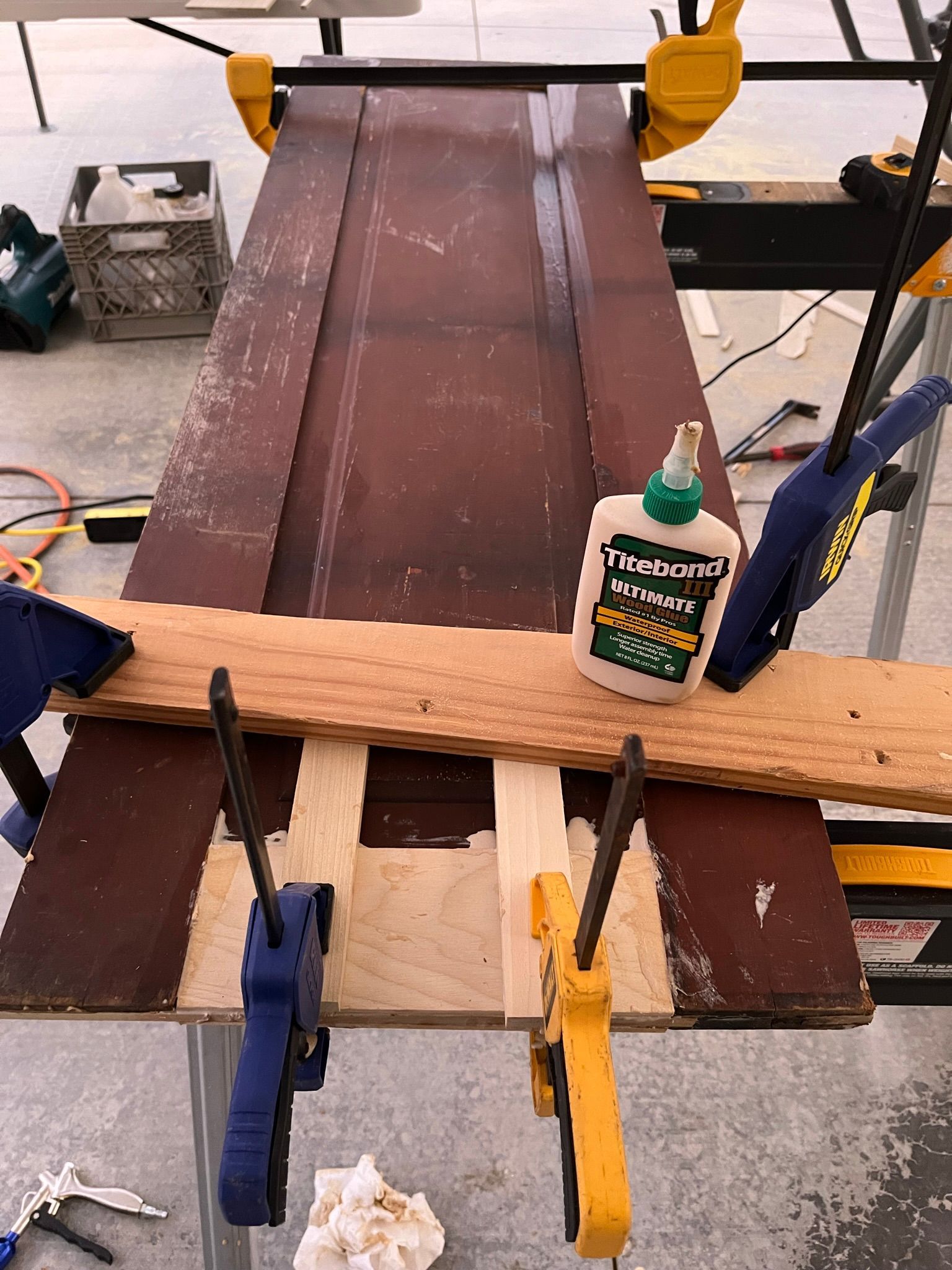 Wood door being repaired with clamps and wood glue on a workbench.