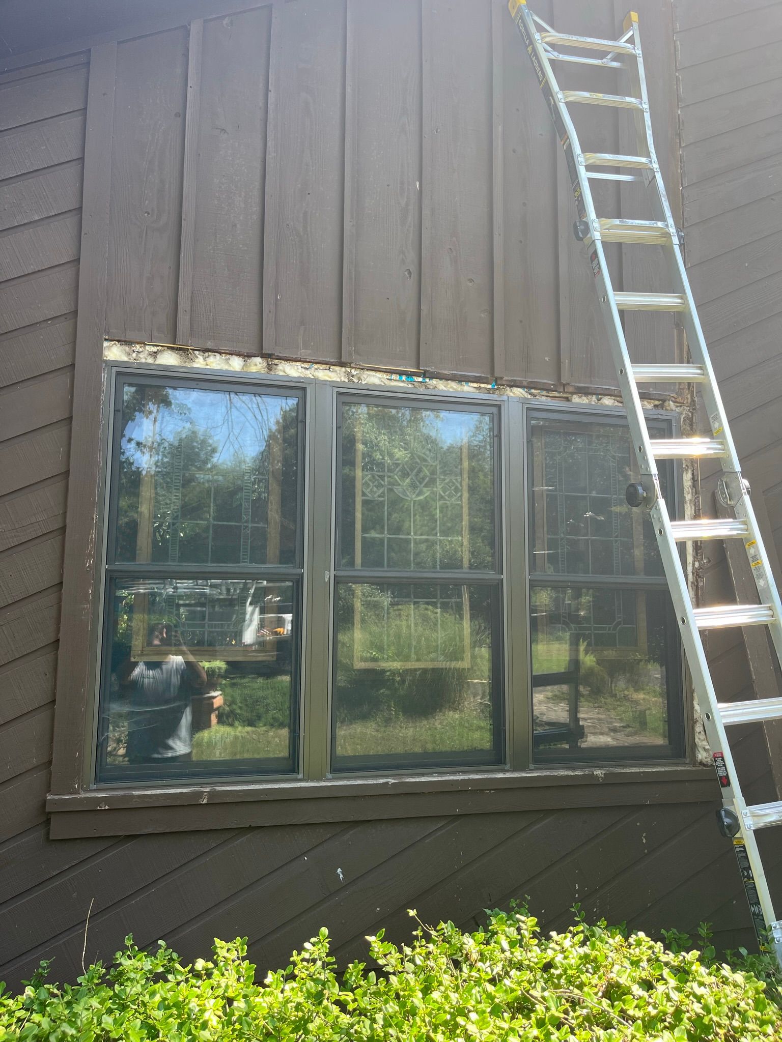 Brown house exterior with ladder next to a three-pane window.