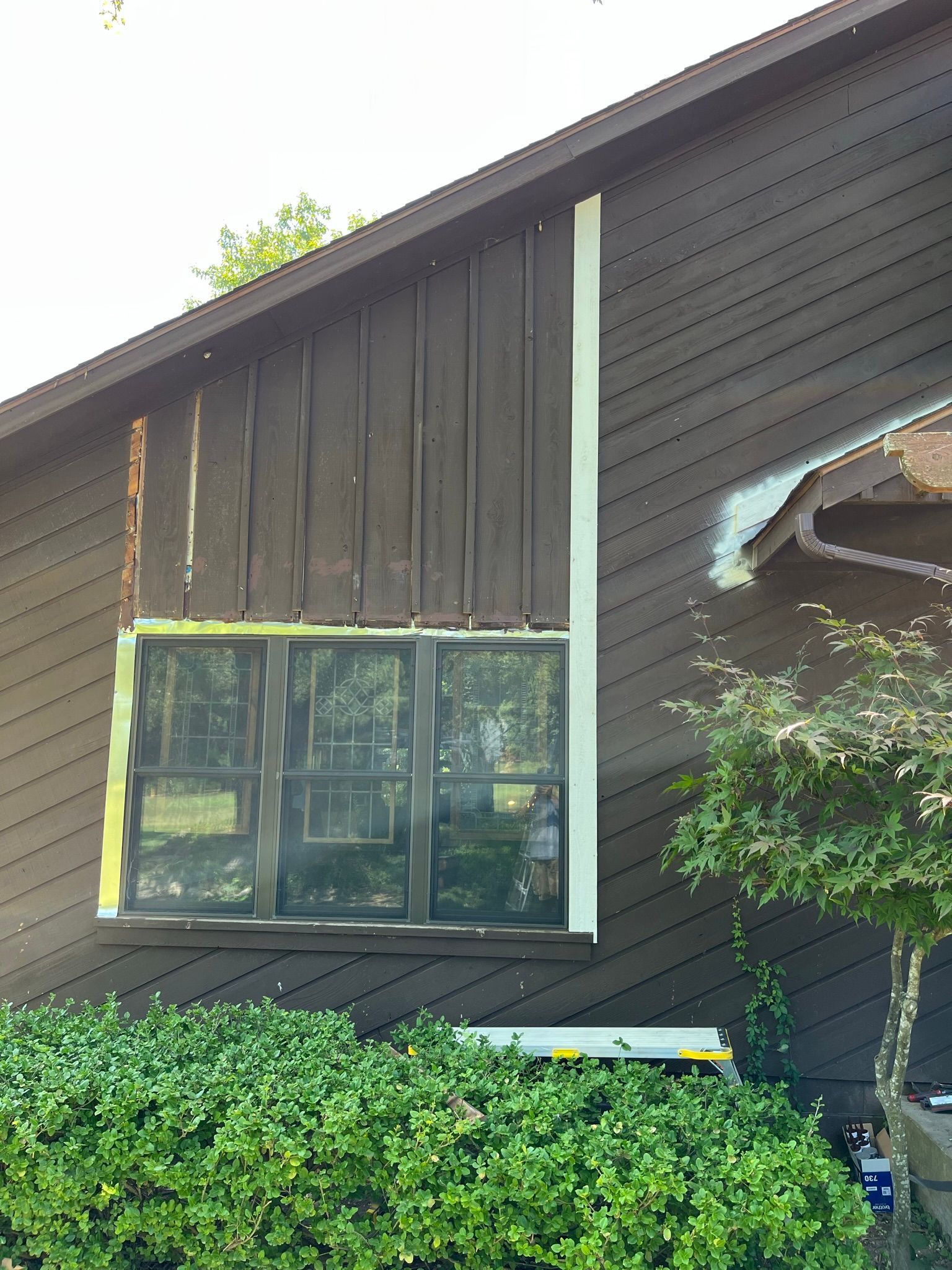 Brown house with removed siding around a window and white trim.