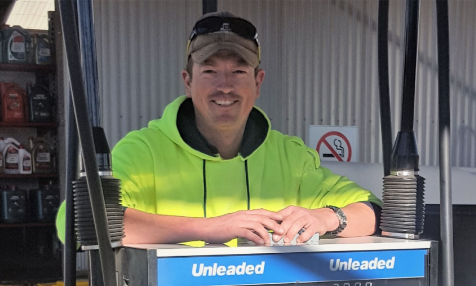 A man is leaning on a gas pump that says unleaded on it.