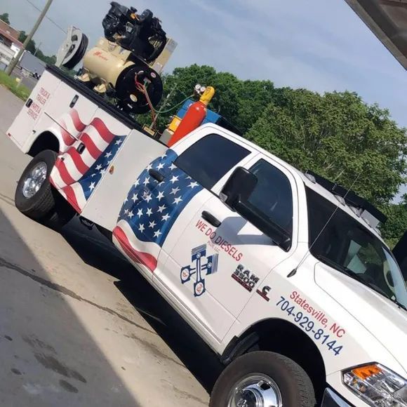 White RAM truck with US flag decal, equipment in bed, Statesville, NC phone number on side.