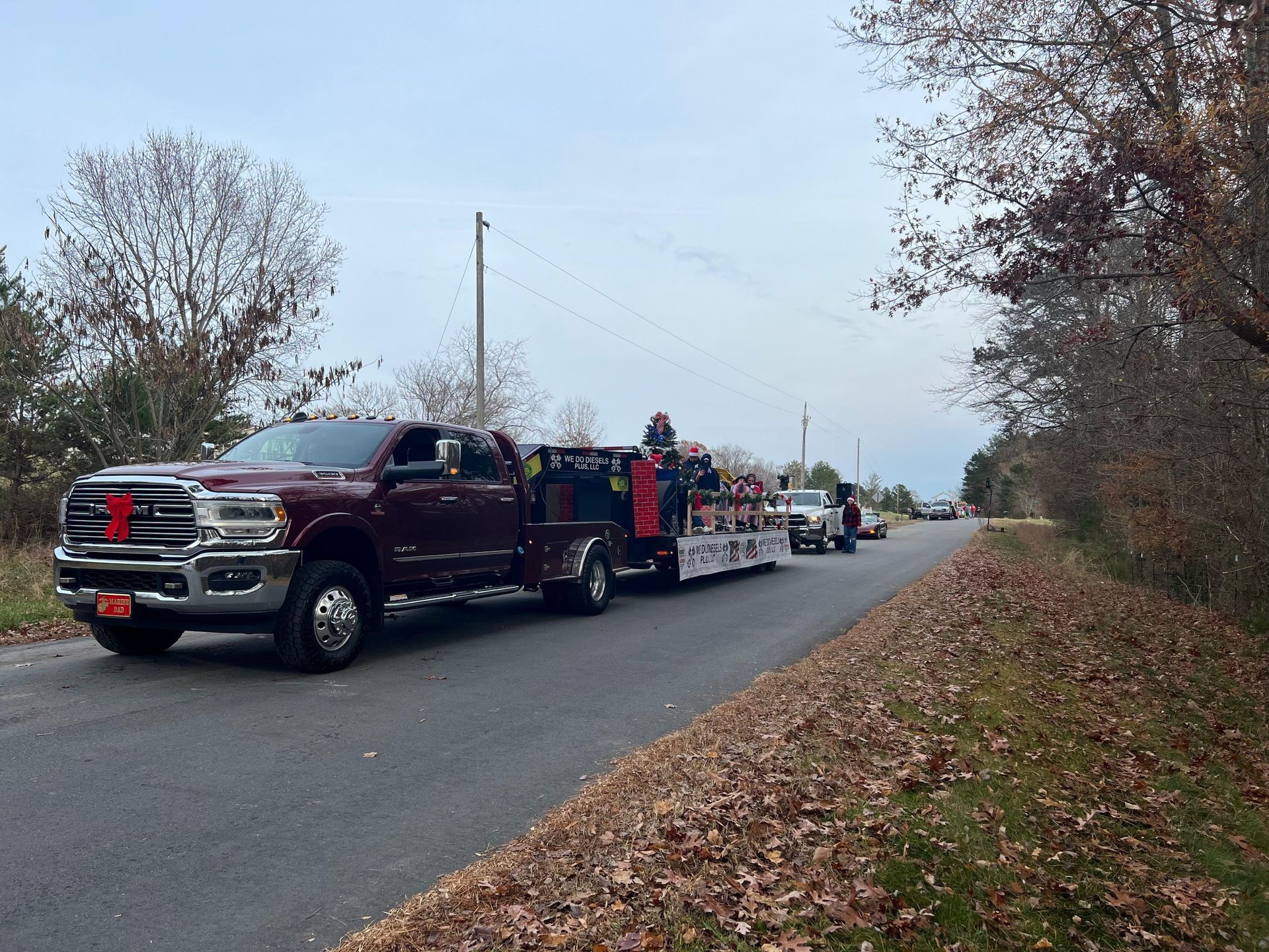Maroon pickup truck towing trailer with items, parked on a road with other vehicles.