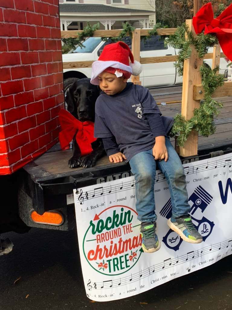 Child in Santa hat and black dog on a decorated truck for a Christmas parade.