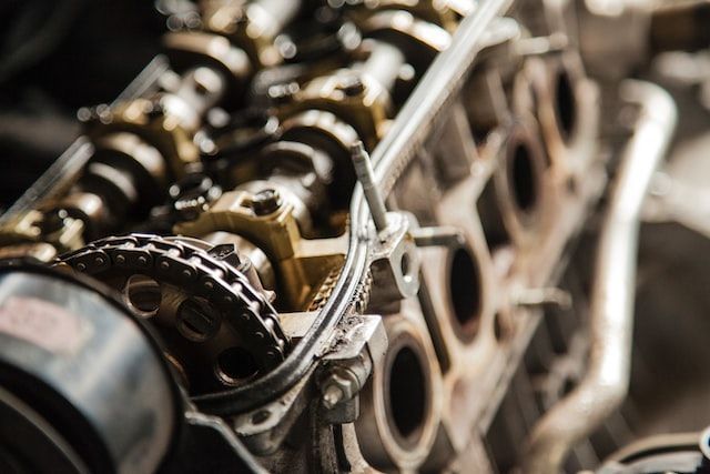 Engine parts, including a chain, gears, and cylinders, with a metallic finish, close-up shot.