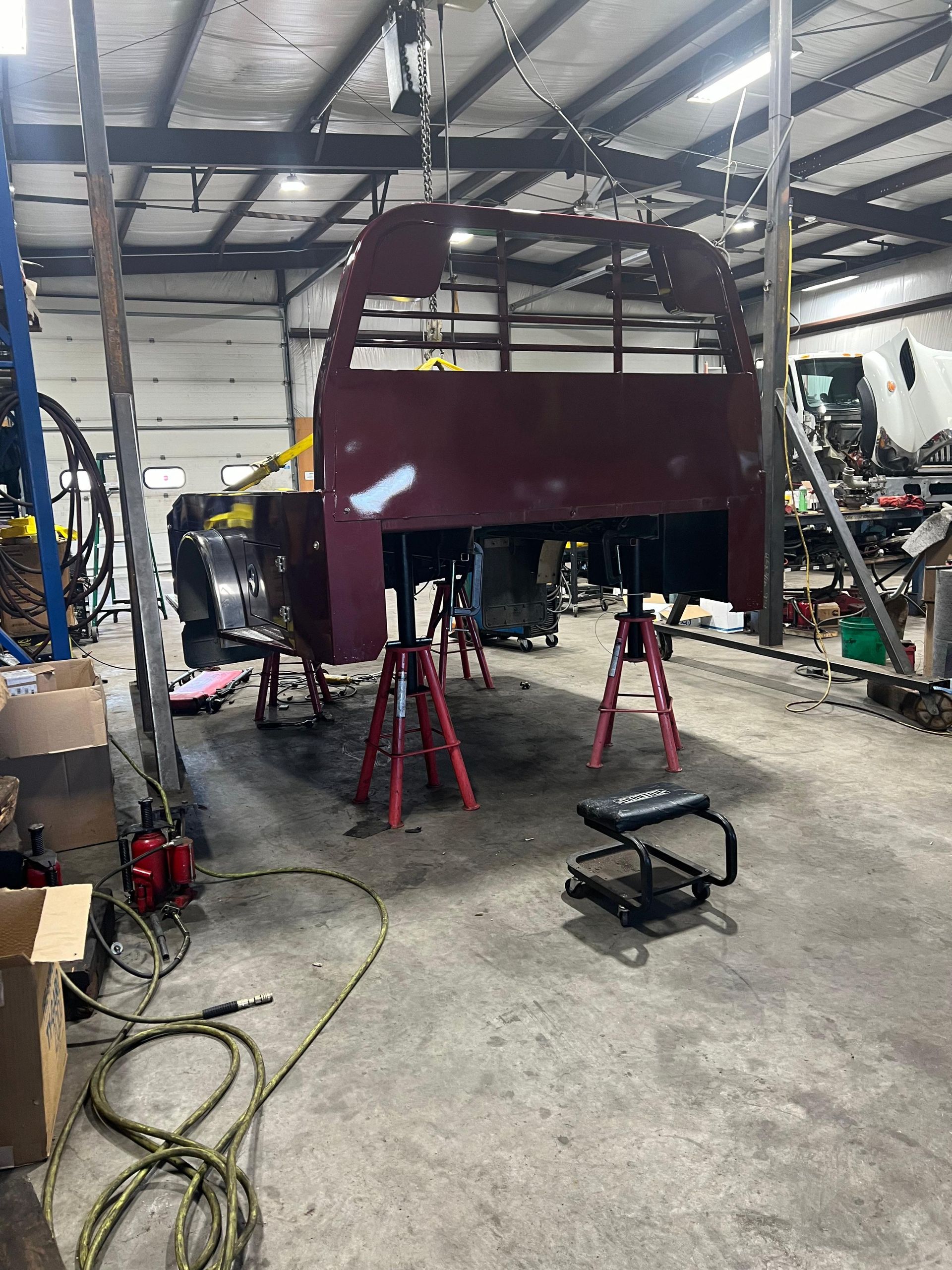 Large burgundy vehicle frame suspended in a workshop, supported by red jack stands.