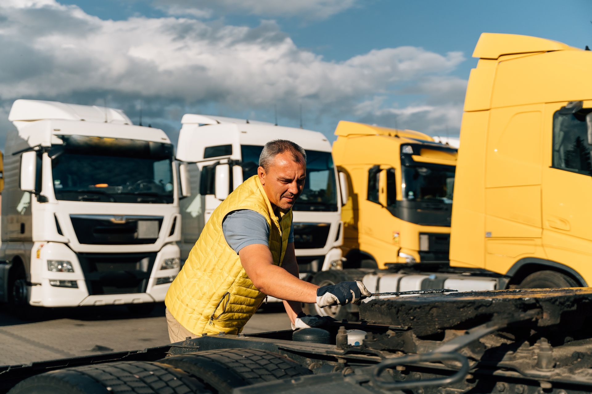 Truck driver inspecting an engine in a lot with white and yellow trucks in the background