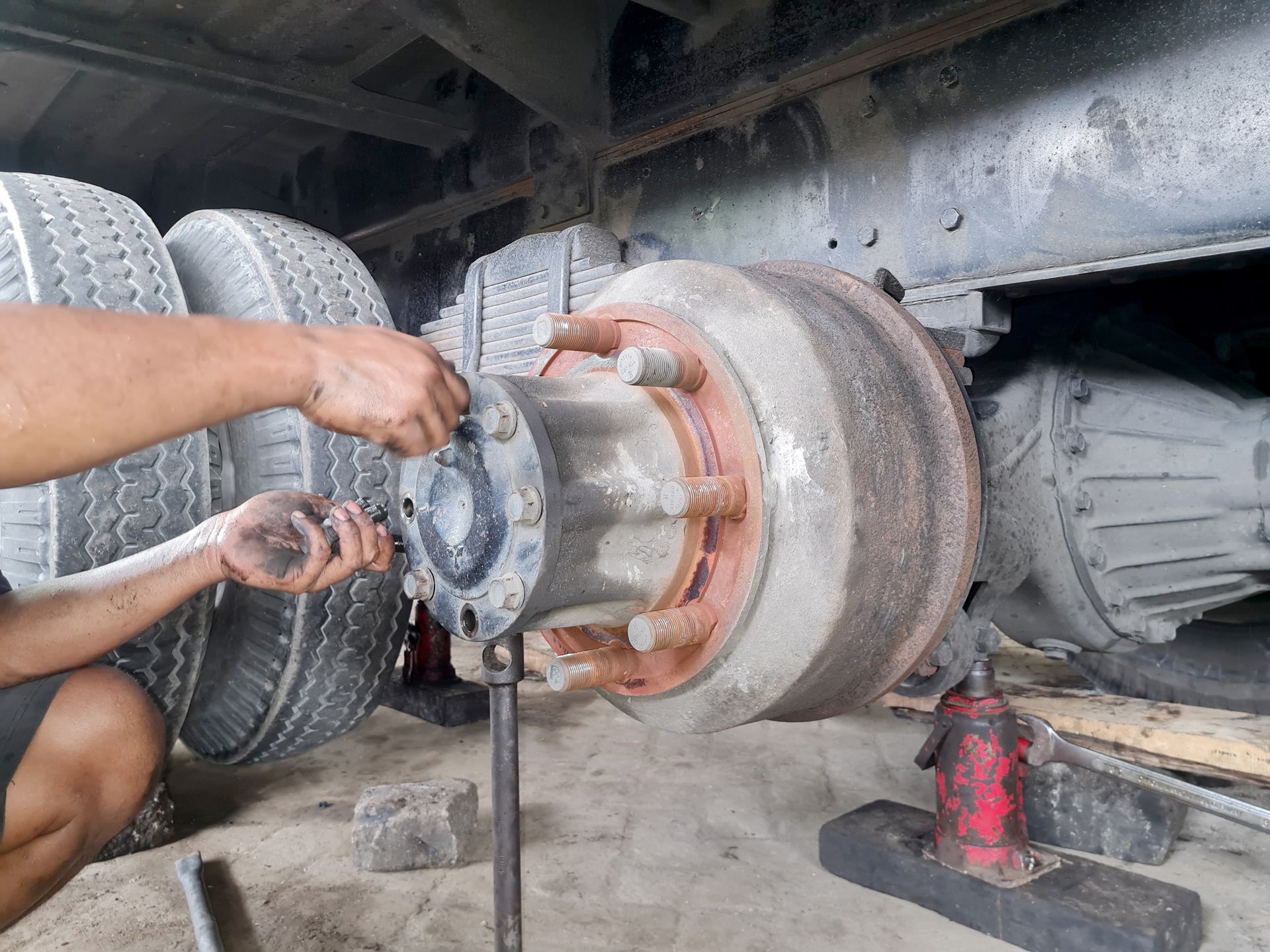 Mechanic repairing a truck wheel hub with tools under the vehicle