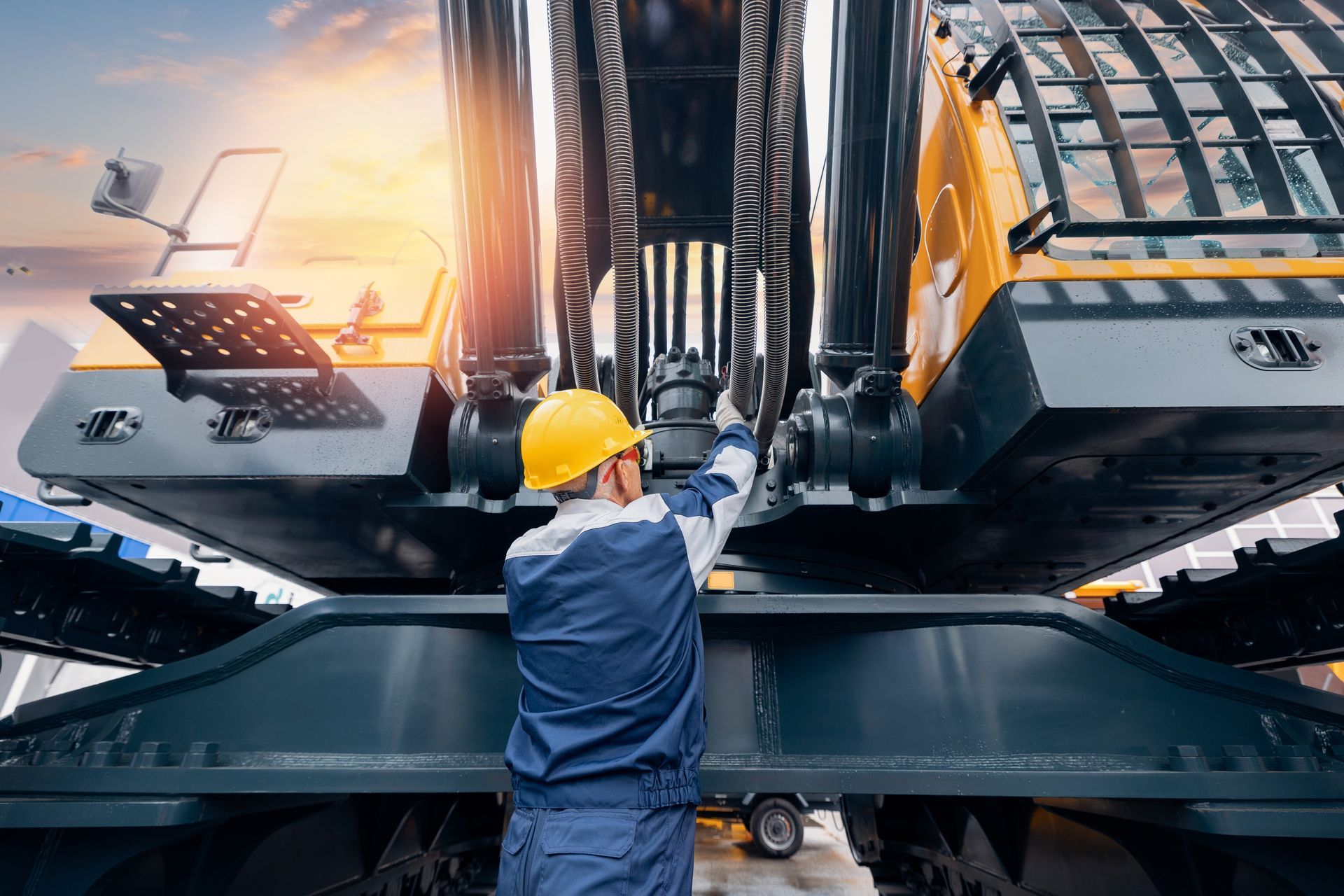 Worker in yellow hard hat inspecting a large industrial machine at sunset