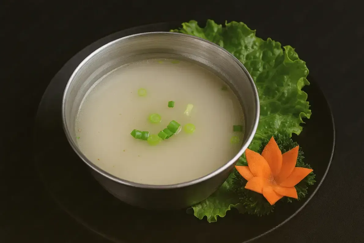 Bowl of creamy soup garnished with green onions, served on a black plate with lettuce and carrot flower garnish