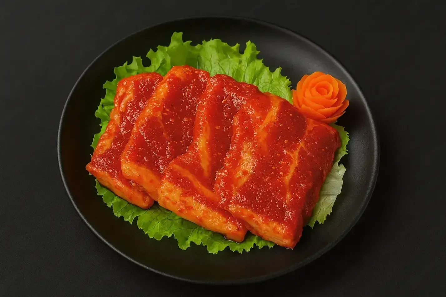 Slices of glazed red meat on lettuce in a black plate, with a carrot rose garnish
