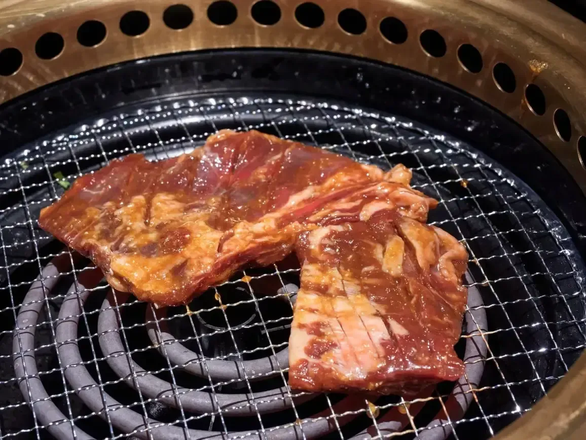 Raw marinated meat cooking on a grill over glowing coals