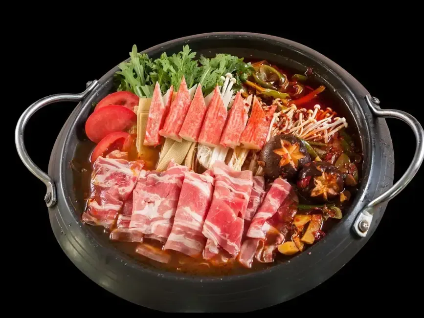 Hot pot with sliced beef, crab sticks, mushrooms, and vegetables in a black pot