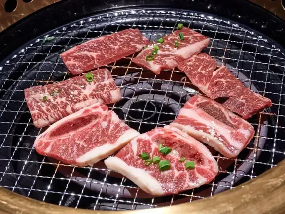 Sliced raw beef grilling on a round barbecue grate, topped with chopped green onions