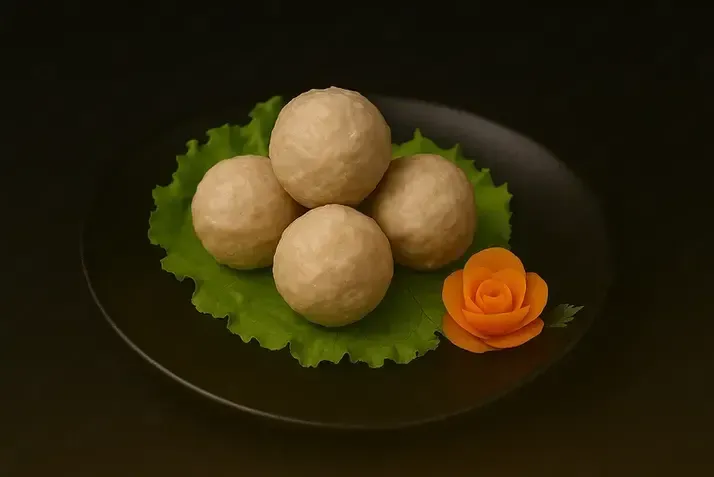 Four beige round sweets on lettuce leaves, garnished with an orange rose on a dark plate