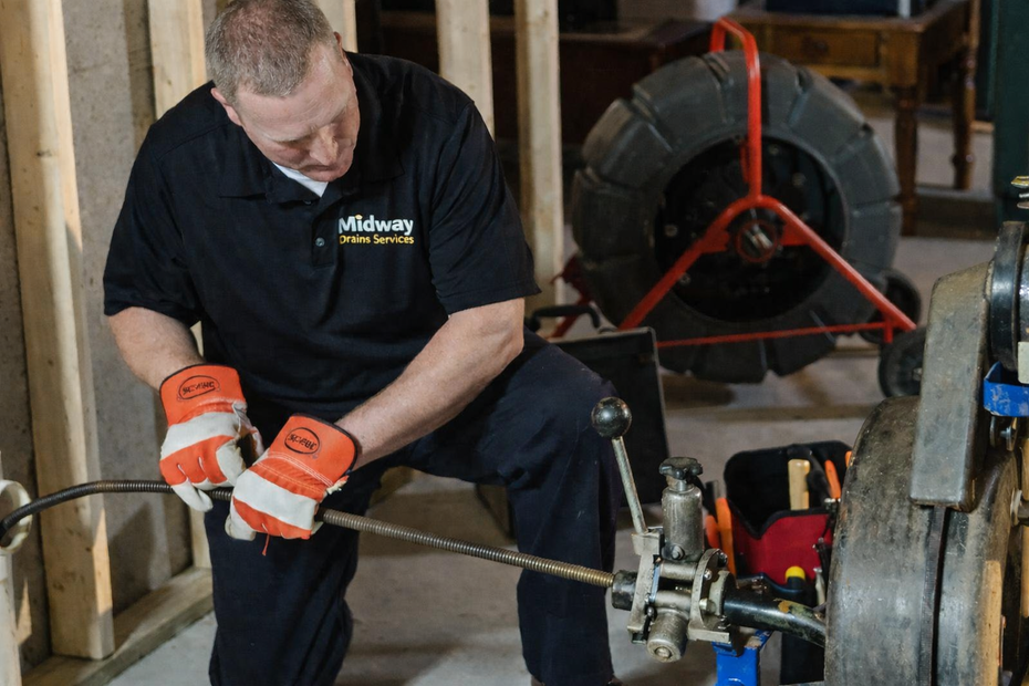 A technician in a high-visibility jacket inspects red fire sprinkler pipes in an industrial mechanical room.