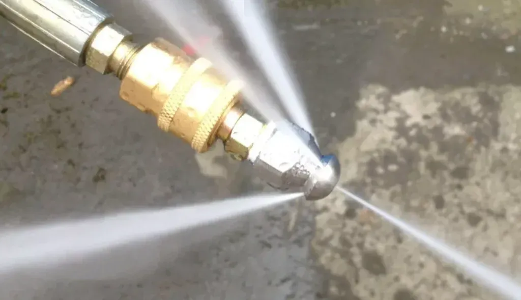 A metal pressure washer nozzle spraying multiple streams of water onto a paved surface.