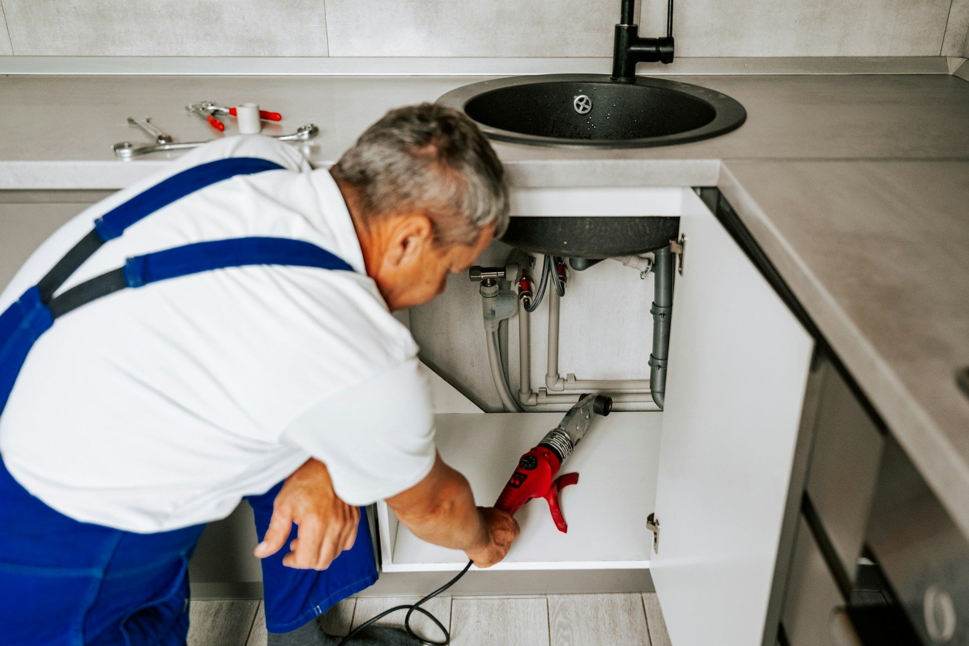 A technician wearing a blue hard hat and safety glasses uses a wrench on pipes connected to an orange expansion tank.