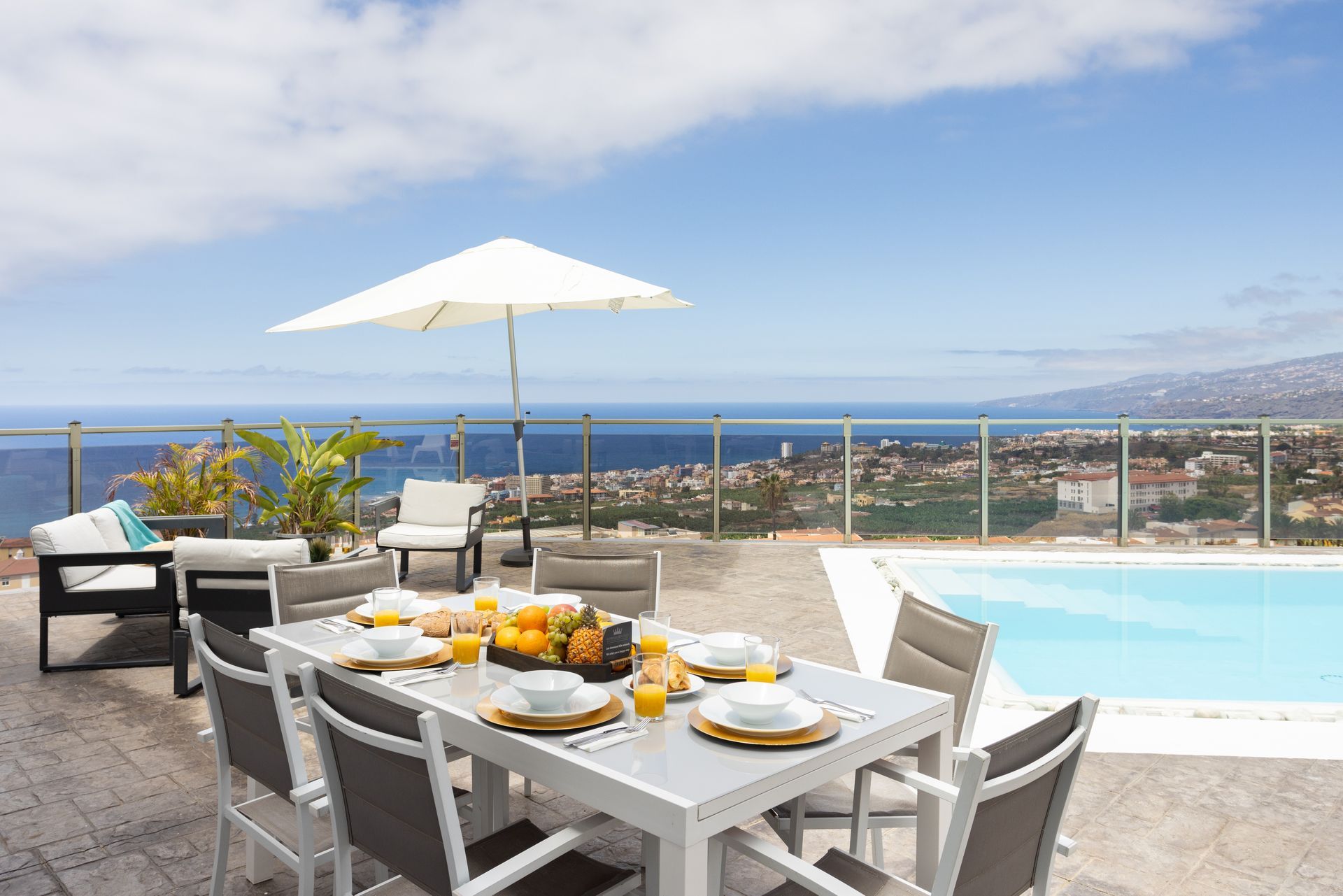 Poolside patio with white table setting, umbrella, lounge chairs, and ocean view