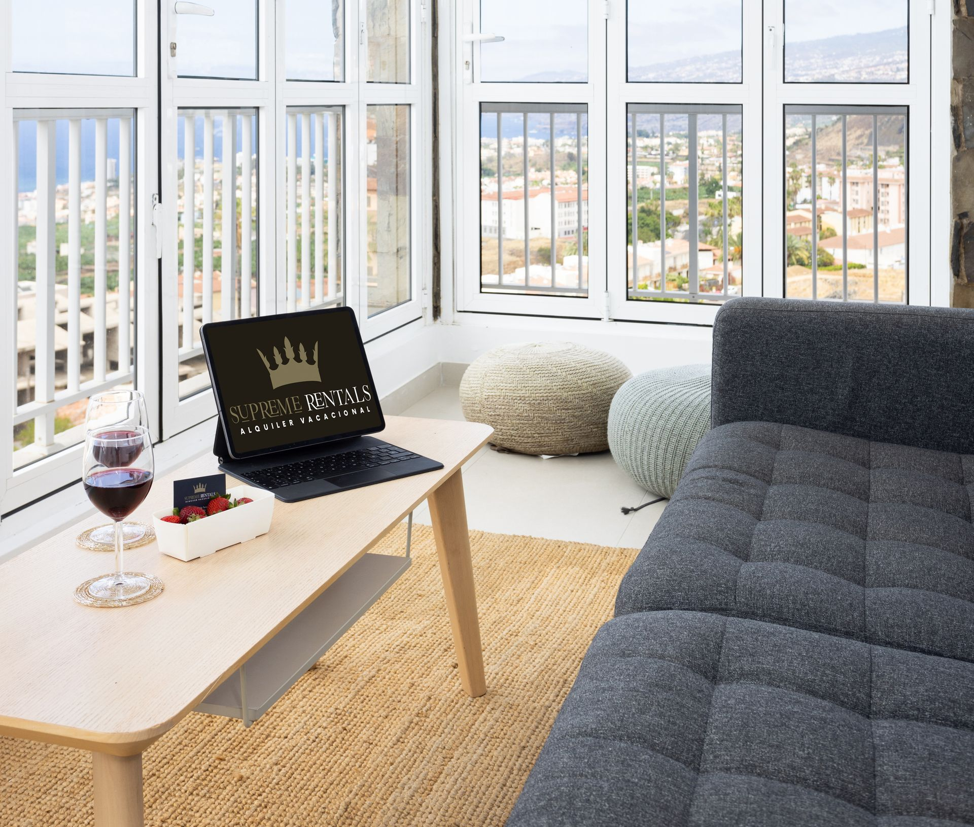 Bright living room with large windows, gray sofa, coffee table, laptop, and cushions by the water.