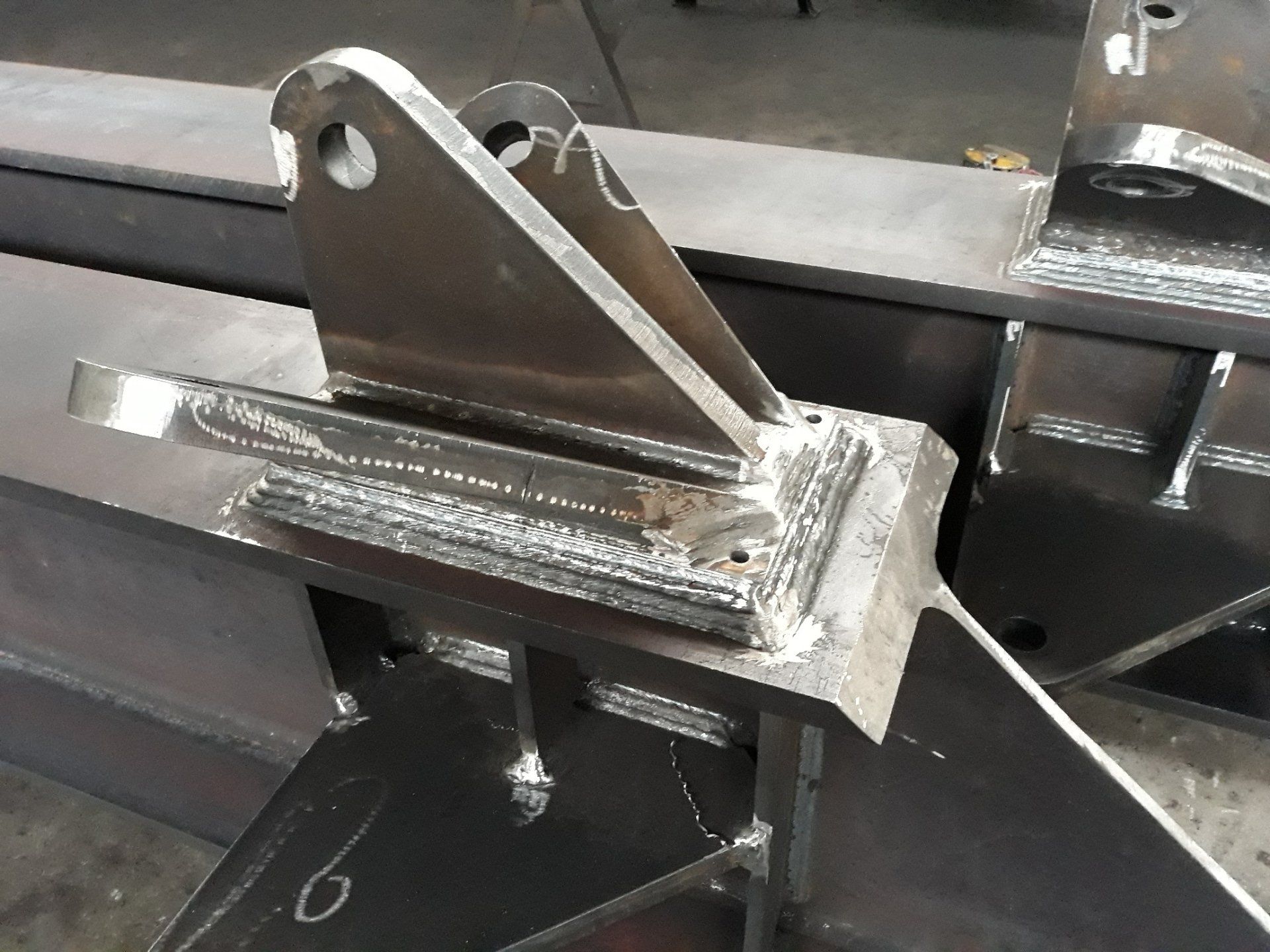 Primo piano di una staffa di montaggio industriale in acciaio grigio scuro saldata su una grande trave metallica in un'officina.