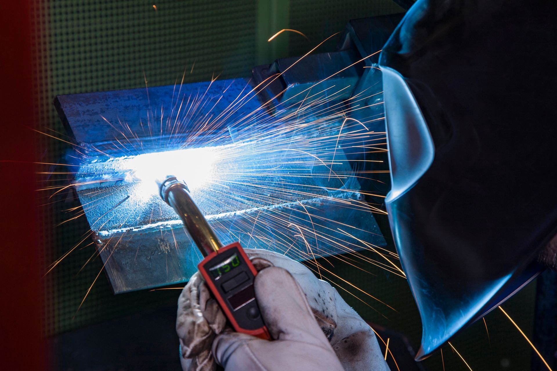 Un saldatore con indumenti protettivi utilizza una torcia per saldare per unire il metallo, creando un arco luminoso e spruzzando scintille.