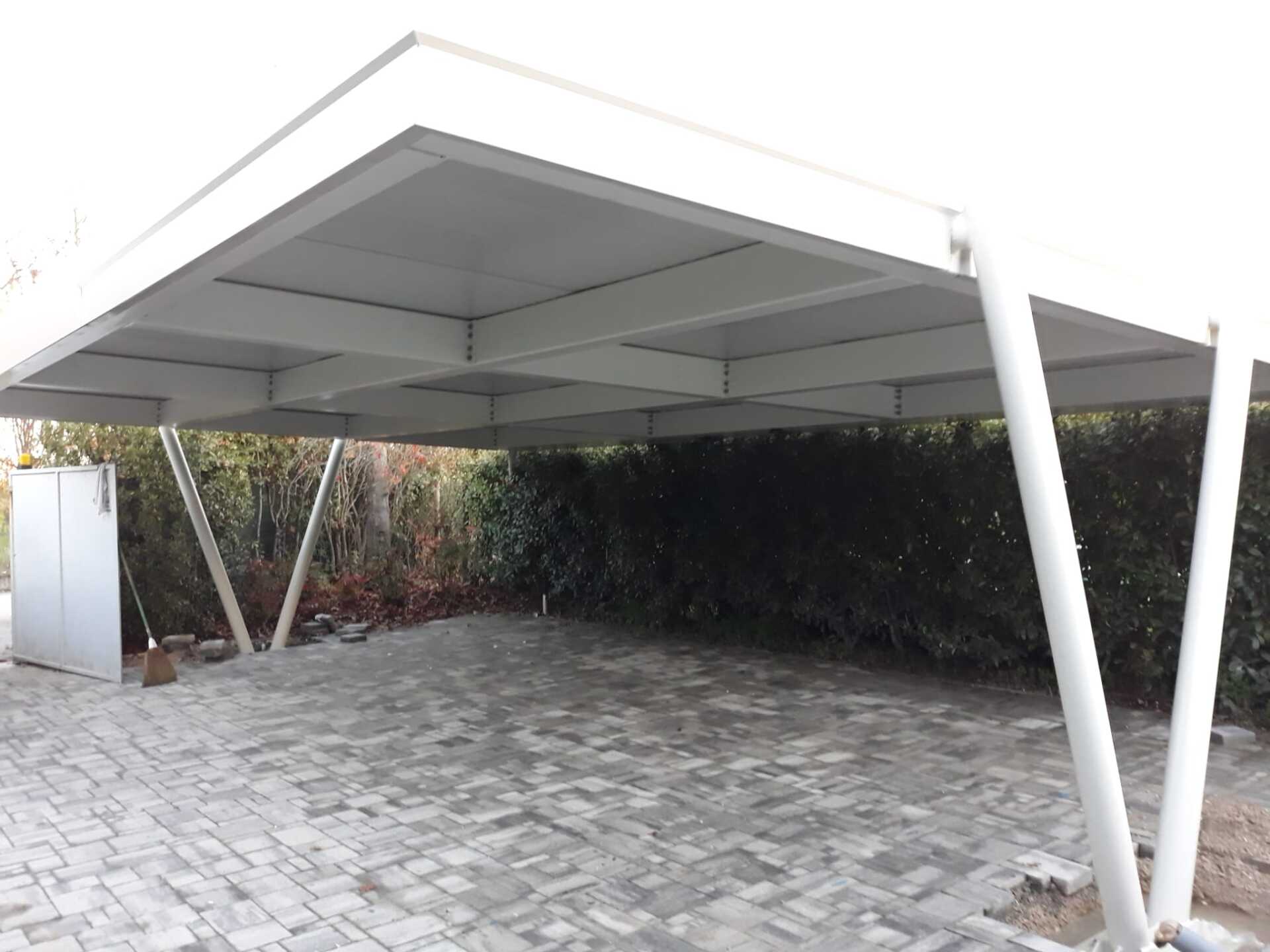 Una moderna tettoia in metallo bianco si erge sopra un vialetto lastricato in pietra, di fronte a una fitta siepe verde.