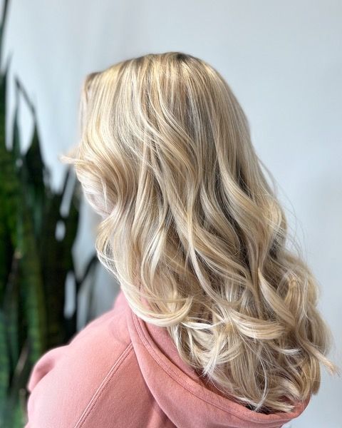 Blonde wavy hair styled in loose curls over a pink top, shown from the back and side.