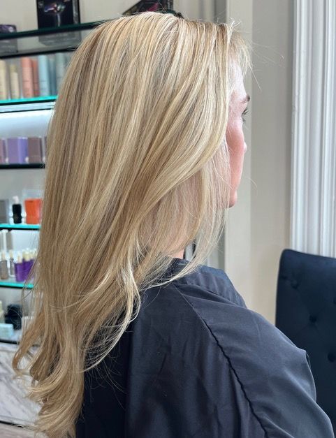 Blonde shoulder-length hair with soft waves, shown in profile against a salon background.