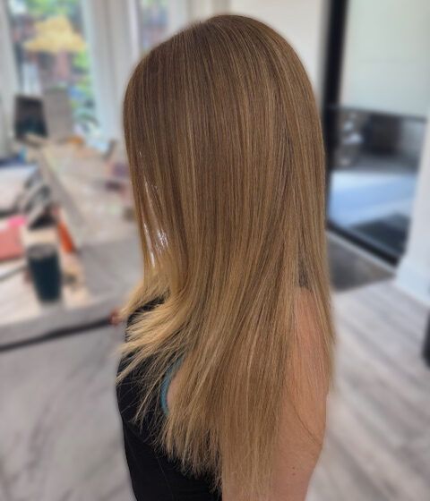Side view of long, straight blonde hair in a salon chair, showing layered ends and subtle highlights
