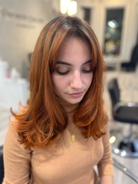 Woman with shoulder-length auburn hair looking down in a salon, wearing a beige top.