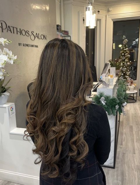 Woman with long wavy brown hair seated in a bright salon