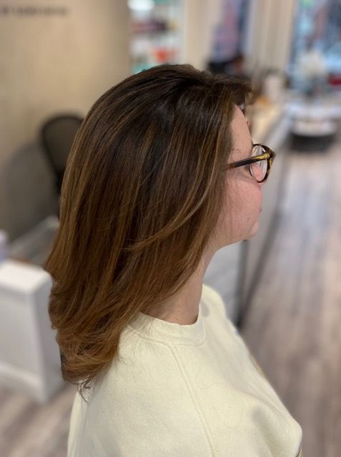 Side profile of a person with brown hair and glasses in a cream sweater inside a salon.