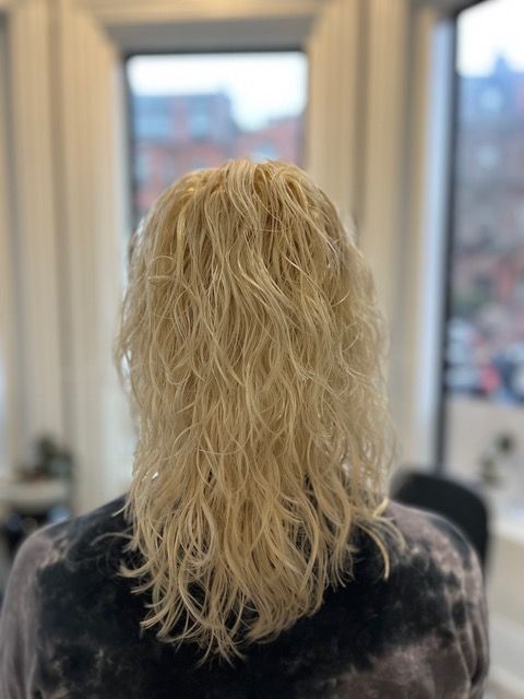 Back view of shoulder-length wavy blonde hair in a salon chair
