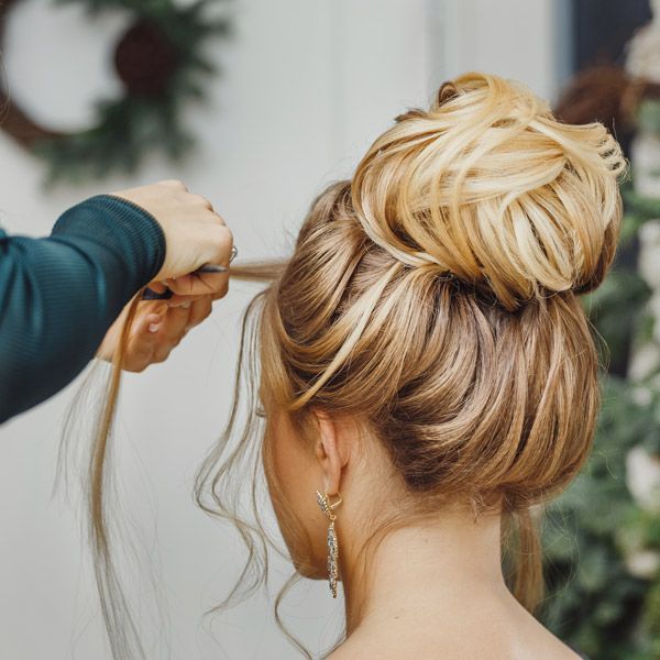 Hairdresser styling a blonde updo with curling iron in a salon
