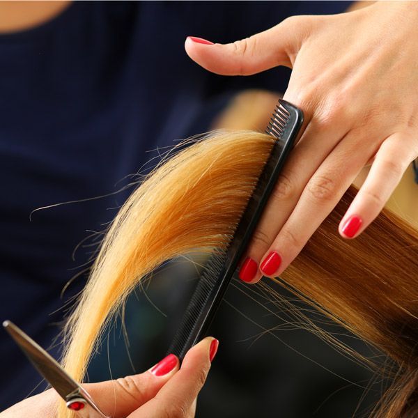 Hands trimming orange hair with black scissors and comb, red nails visible