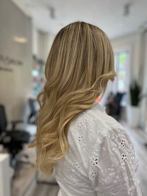 Blonde hair styled in loose waves, shown from behind in a salon setting