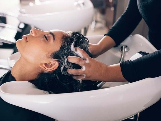 Woman getting her hair washed in a white salon sink by a stylist wearing black gloves
