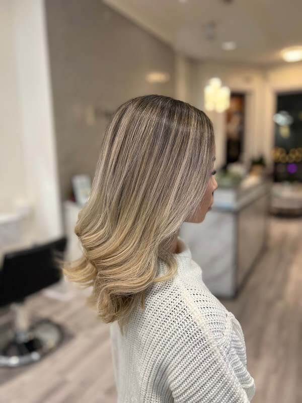Blonde shoulder-length layered haircut with soft curls in a salon setting