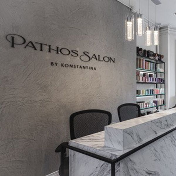 Pathos Salon reception with marble counter, black chairs, and product shelves against a gray wall
