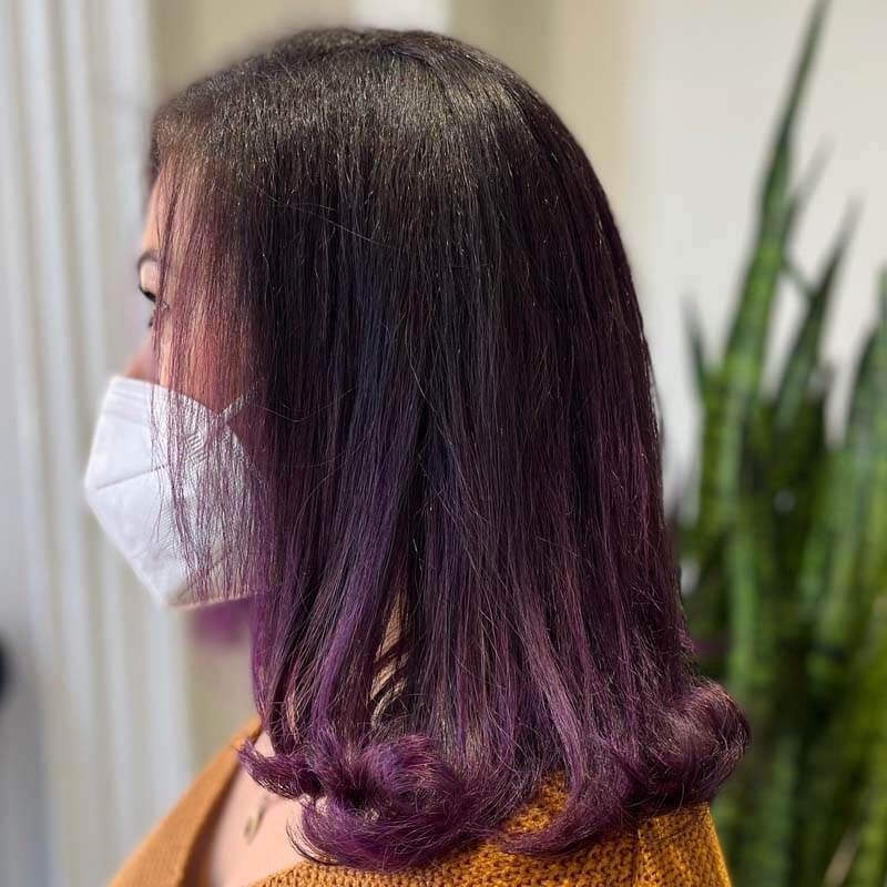Side view of a person with dark-to-purple ombré hair wearing a white face mask