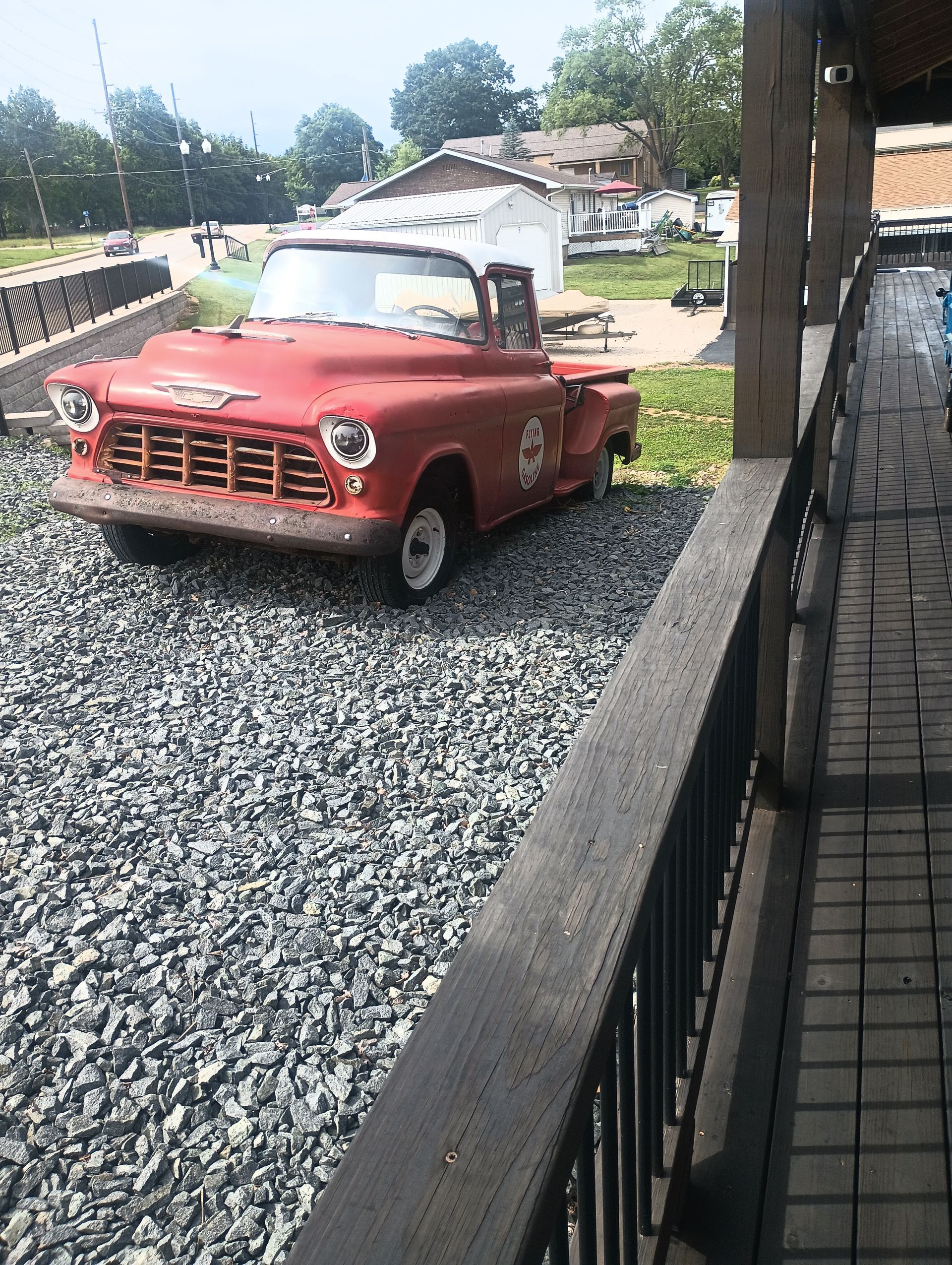 Red vintage car parked on gravel beside a sidewalk and brick wall outdoors