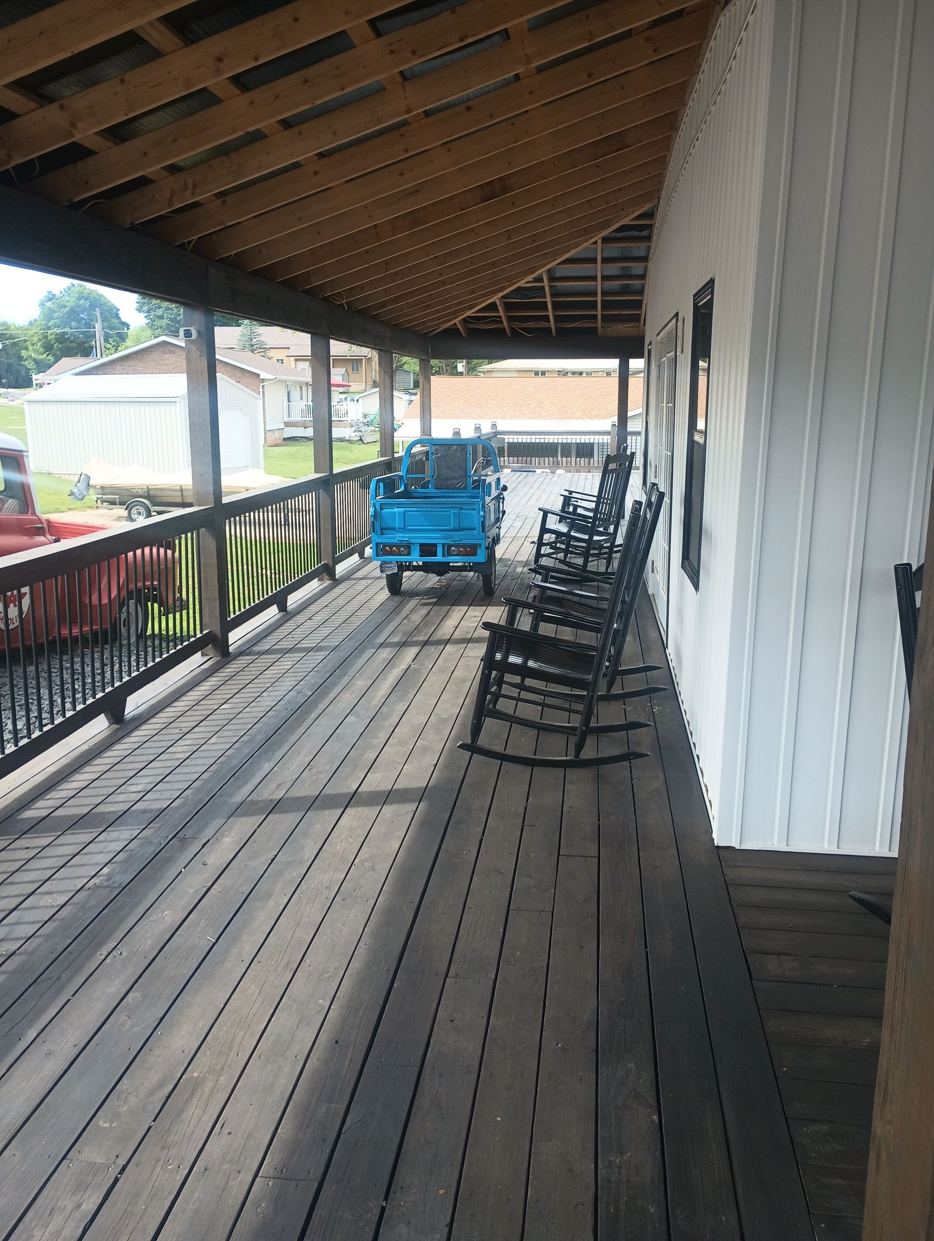 Covered wooden porch with stacked black chairs and a blue cart under a slanted roof.