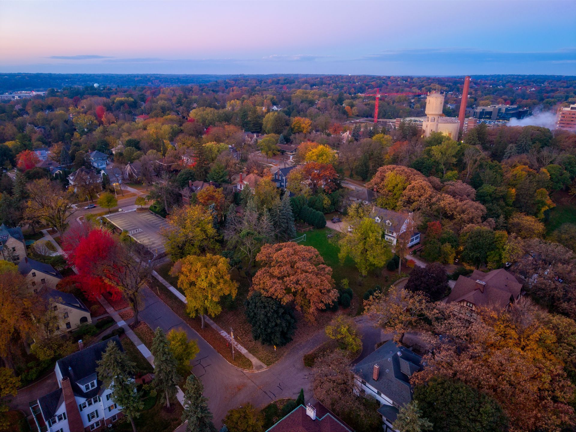 Aerial view of a suburban neighborhood in autumn at sunset with colorful trees and a water tower in the distance