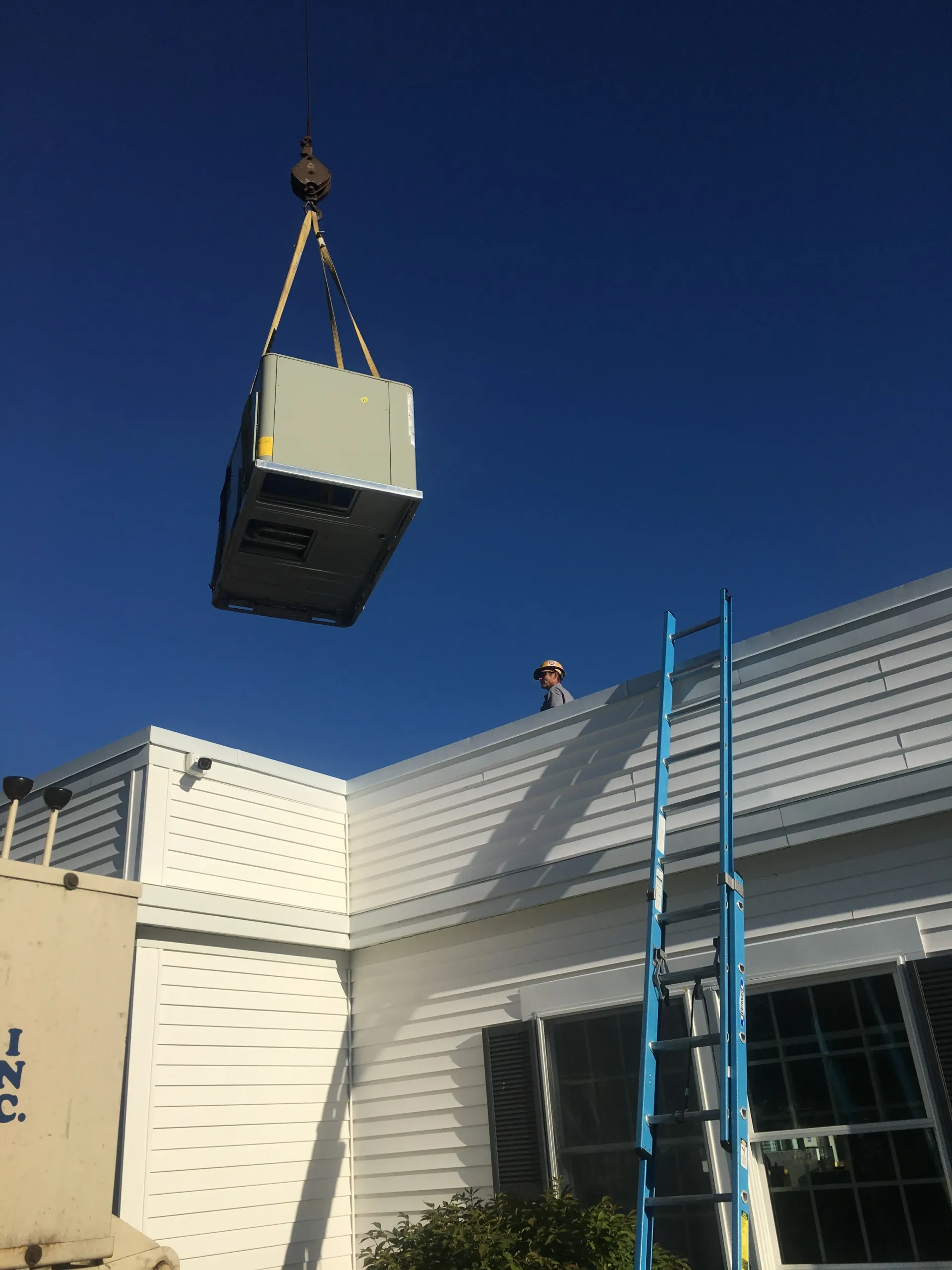 A crane is lifting an air conditioner from the roof of a building.